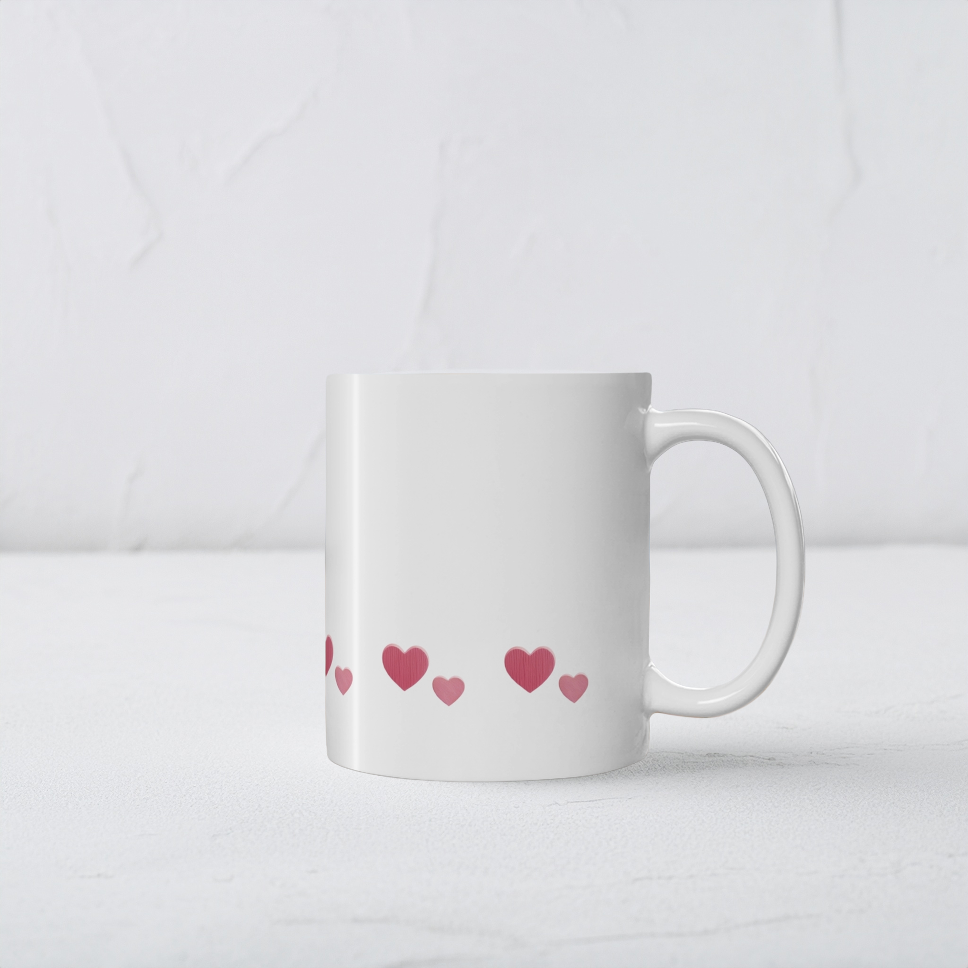 White ceramic mug with row of red hearts wrapping around the mug near the bottom. The mug sits on a white wooden surface