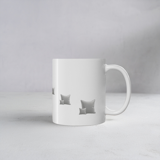A white ceramic mug with a handle, featuring a printed pattern of gray throw pillows on the front, set against a neutral light gray background.