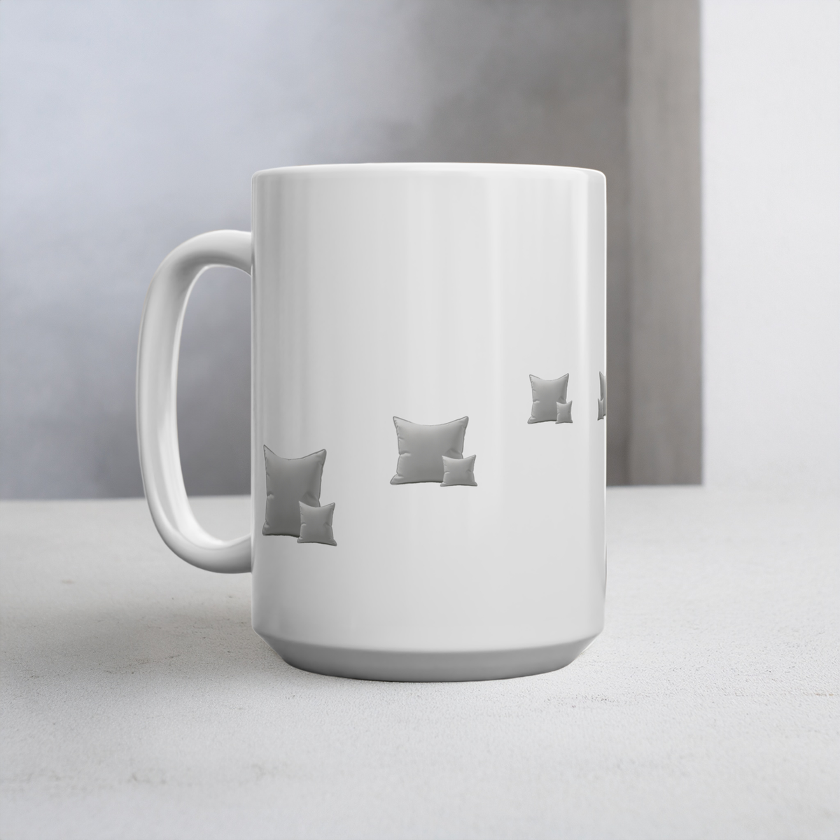 A white ceramic mug with a handle, featuring a minimalist printed design of small grey throw pillows on the side, set against a soft grey background.