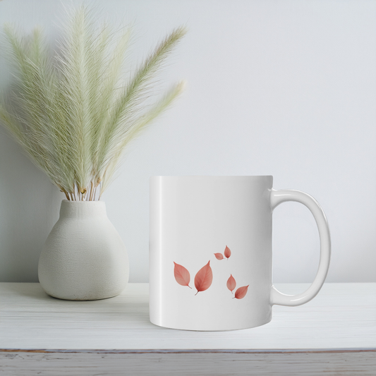 White ceramic mug with red and brown autumn leaf clusters design. The mug sits on white wooden surface.