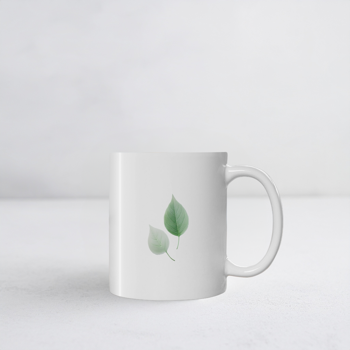 White ceramic mug with two green and white autumn leaf design. The mug sits on white surface.