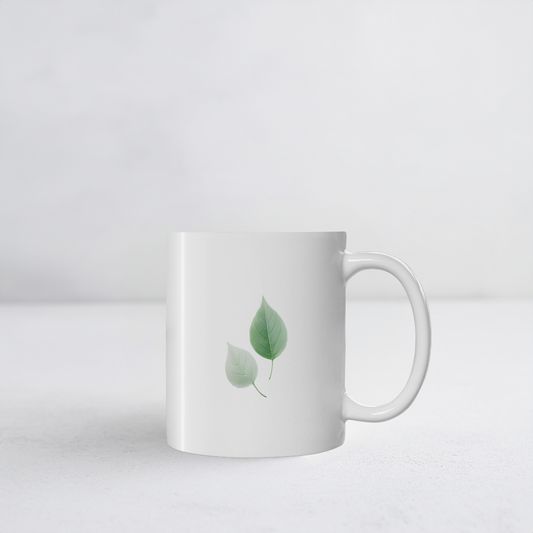 White ceramic mug with two green and white autumn leaf design. The mug sits on white surface.