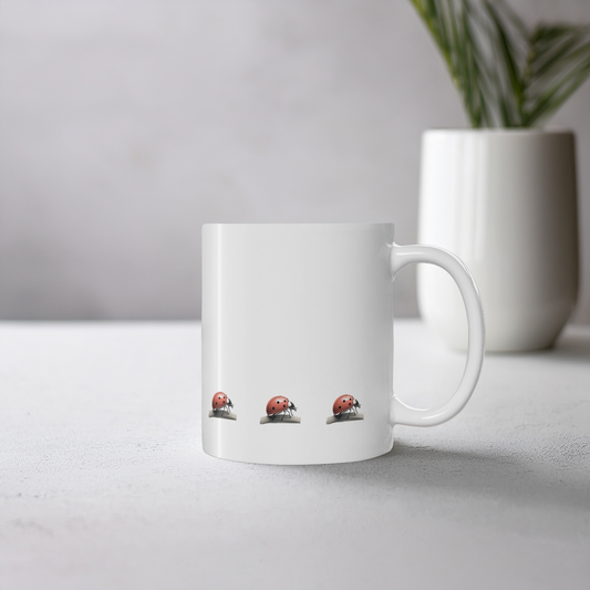 White ceramic mug with red ladybird (ladybug) design. The mug sits on a cement style surface with small plant pot behind it.