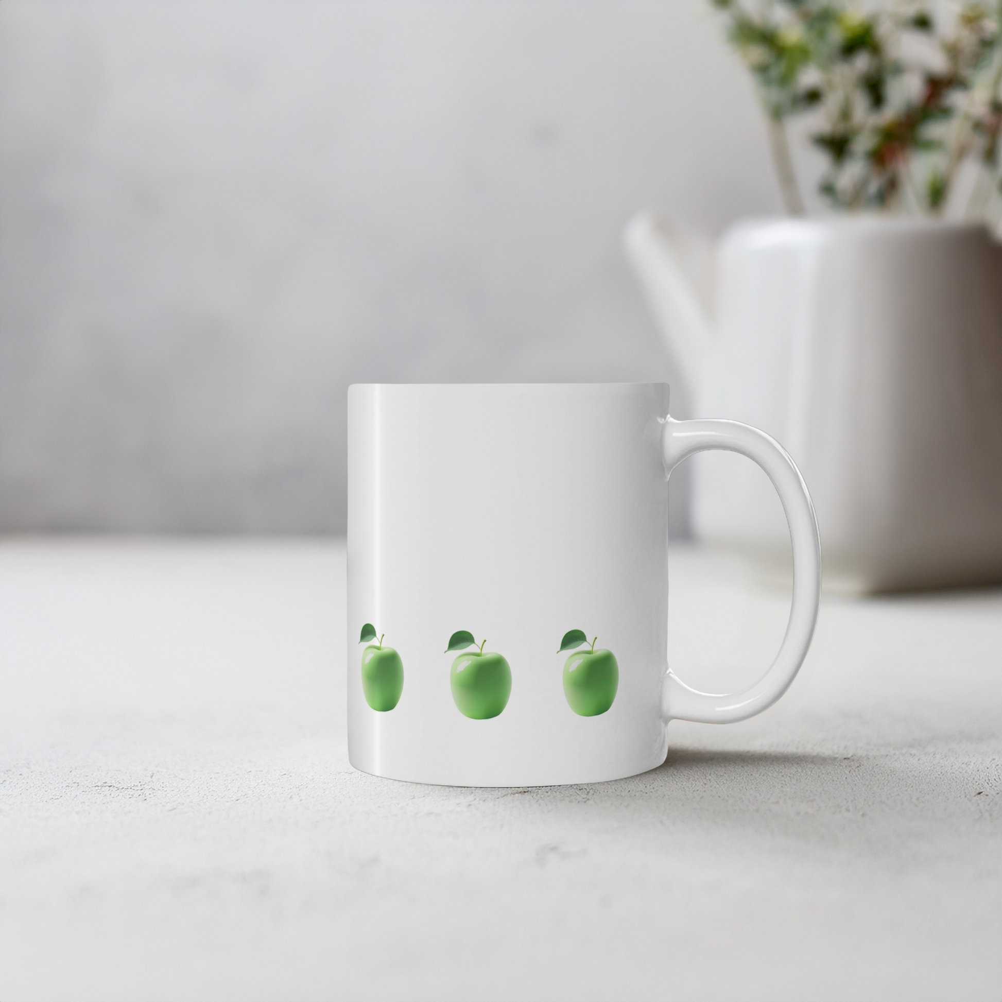 White ceramic mug with green apple design. The mug sits on a cement style surface with small plant pot behind it.