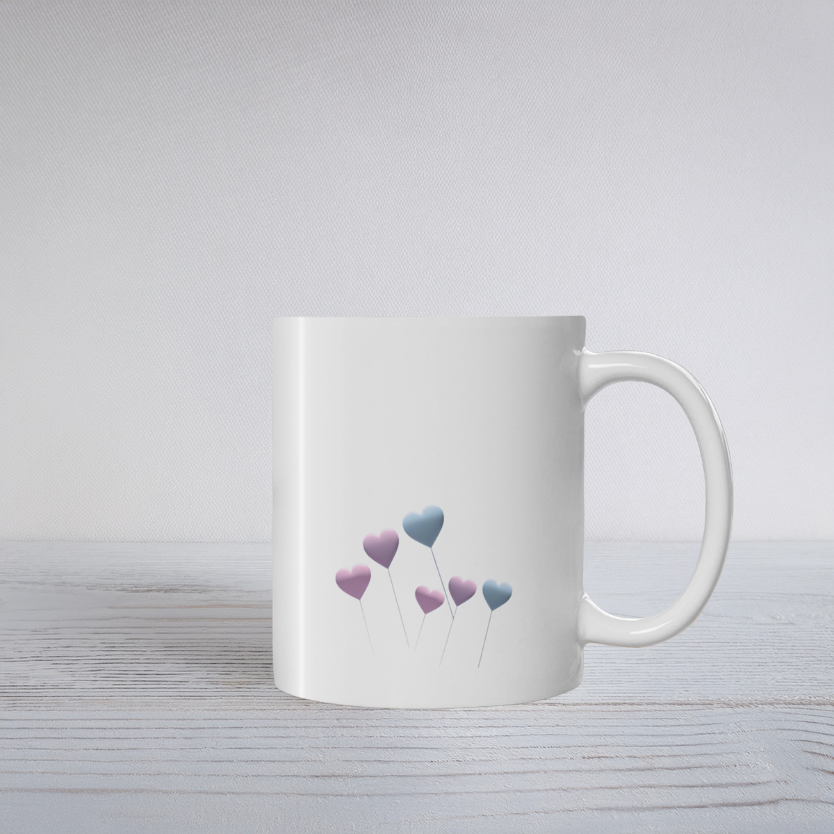 White ceramic mug with pale blue and purple floating heart design on a white wooden surface