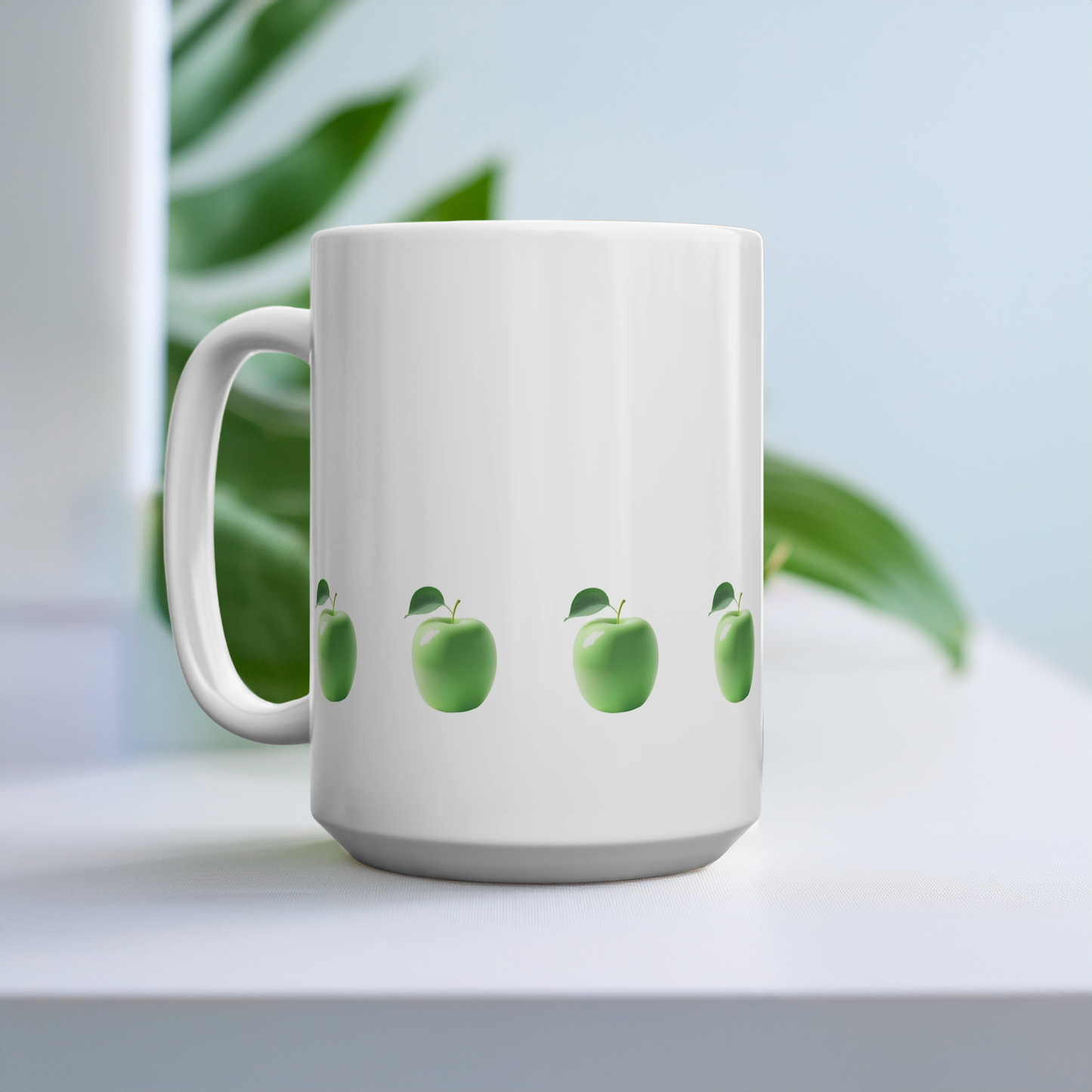 15oz mug with design of row of green apples at the bottom. The mug is on a table with a large plant in the background.
