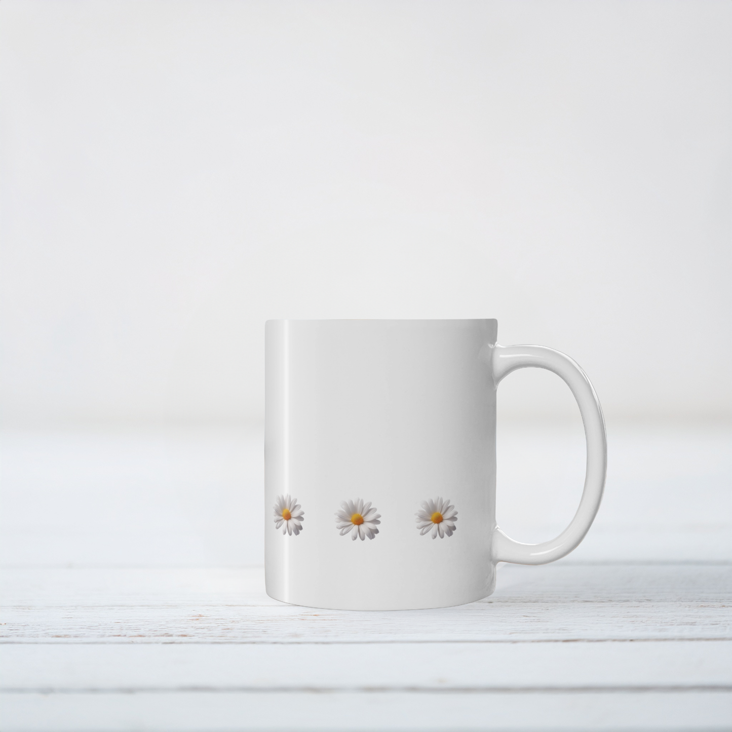 White ceramic mug with daisy design. The mug sits on white wooden surface.