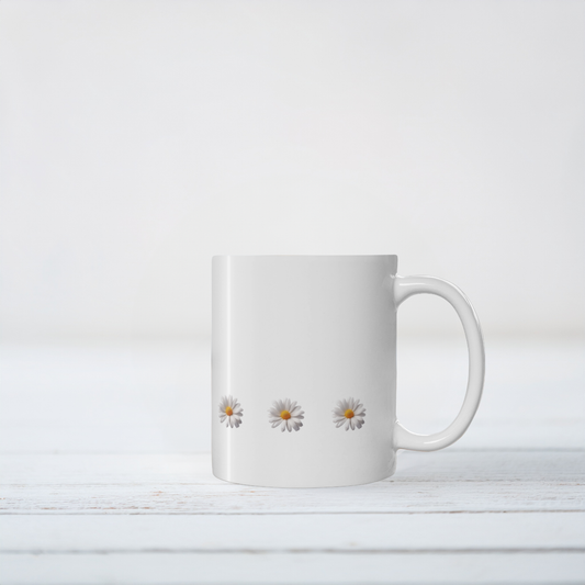 White ceramic mug with daisy design. The mug sits on white wooden surface.