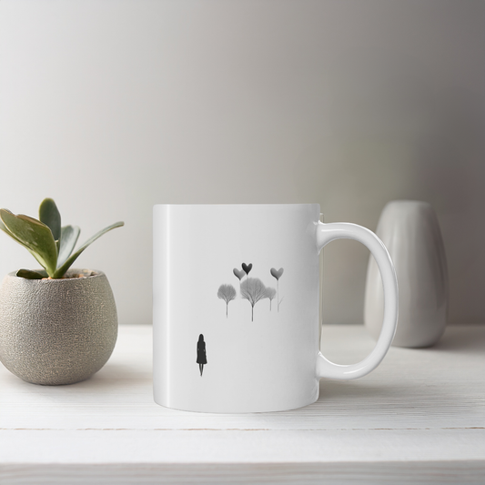 White ceramic mug with black line art illustration of woman and whimsical trees. The mug sits on a white wooden table with small plant pot and ceramic ornament. 